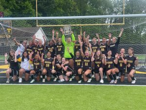 group of young women in soccer uniforms cheering inside of the soccer goal 